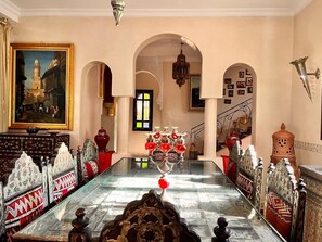 Ein Zimmer mit einem Glastisch, verzierten Möbeln, einem Gemälde einer Moschee und einer Treppe.