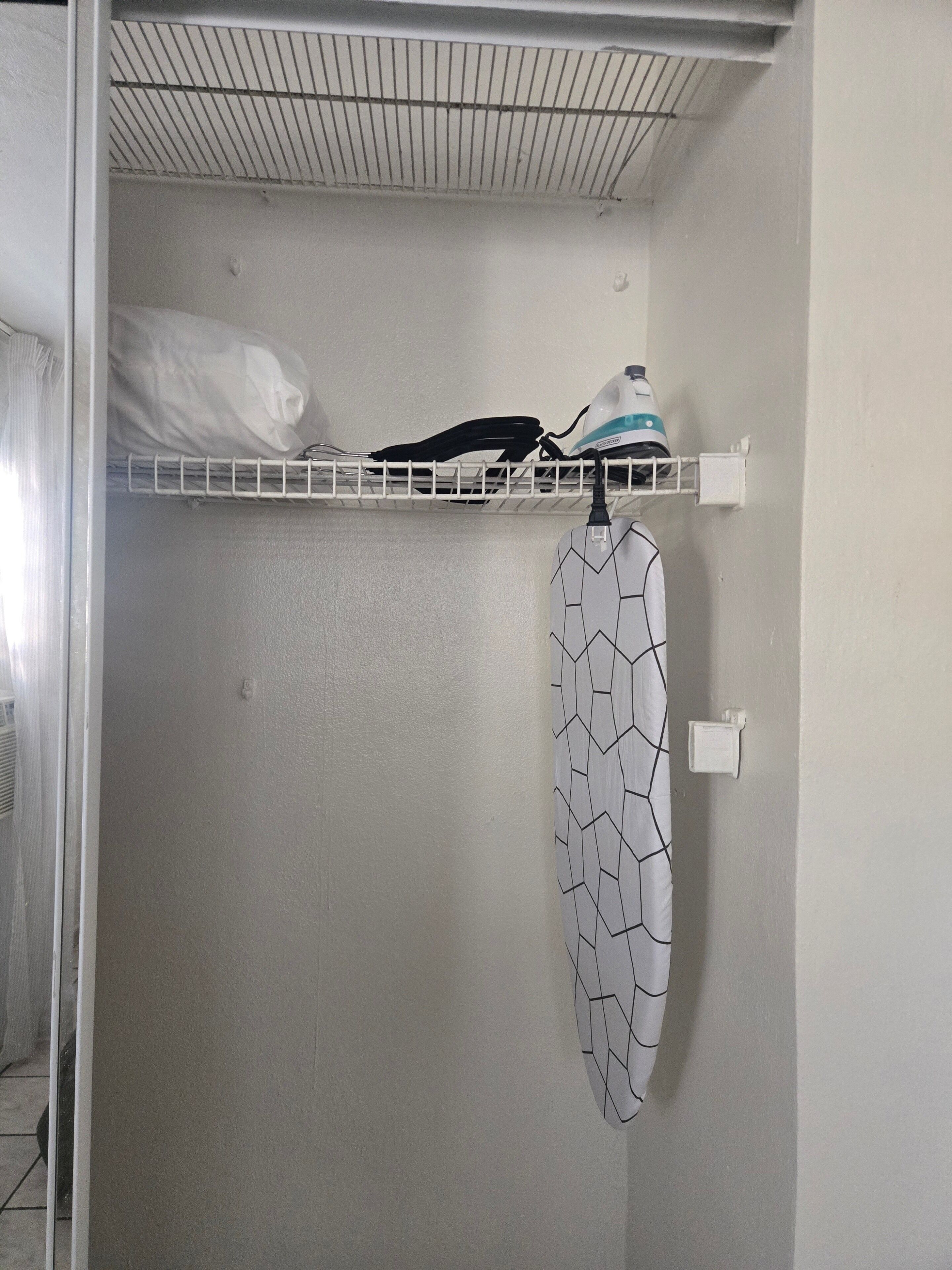A closet with a hanging rack, a shelf with a white pillow and a black object, and a patterned garment.
