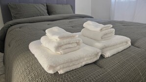 Una cama bien hecha con un cabecero gris y almohadas, junto con dos toallas blancas dobladas sobre la cama.