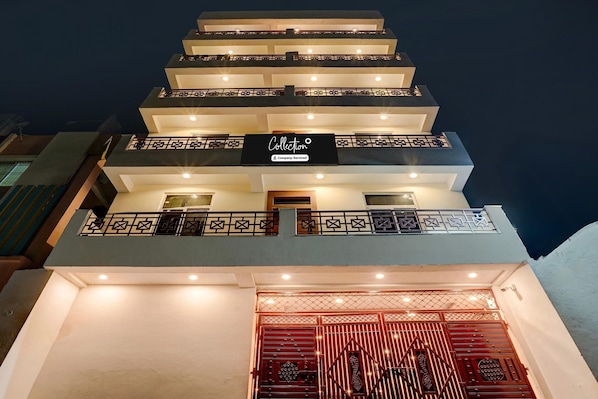 Un immeuble à plusieurs étages, reconnaissable à son panneau indiquant « Collection », doté de balcons avec des garde-corps et d’une entrée fermée par un portail.