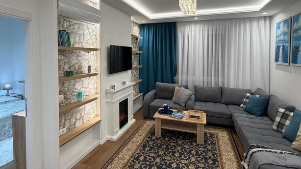 Un salon moderne avec une cheminée, un ensemble de canapés gris, un tapis à motifs et un téléviseur.