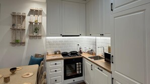 Une cuisine moderne avec des armoires blanches, un four encastré et un coin repas avec une table dressée pour deux personnes.