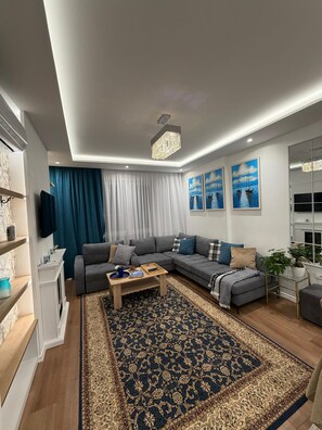 Een moderne woonkamer met een hoekbank, een salontafel, een kamerkleed met patroon, en kunstwerken aan de muur.