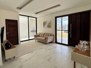 A modern living room with a sofa, a coffee table, a TV, and a sliding glass door leading to an outdoor area. - House with Pool • 10min French • Cond. Closed (Marechal Deodoro)