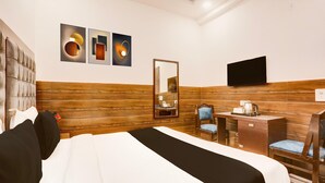 Habitación de hotel con cama, escritorio, silla, espejo y obras de arte en la pared.
