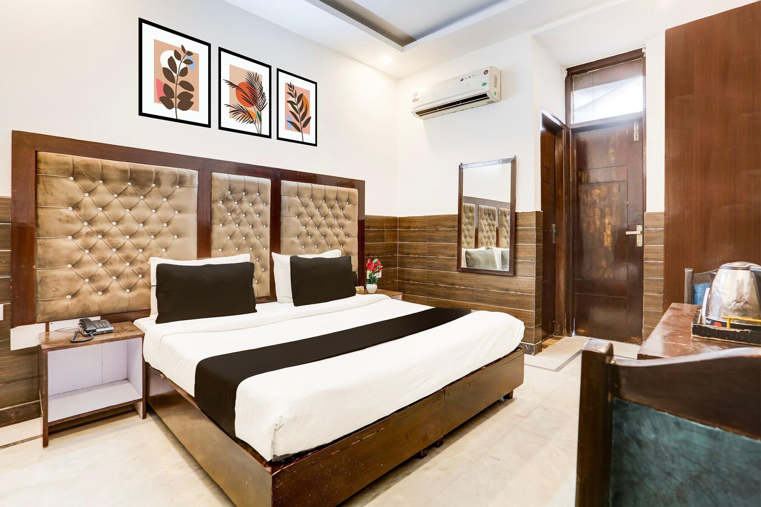 A hotel room with a large bed, a bedside table, a mirror, and framed artwork on the wall.