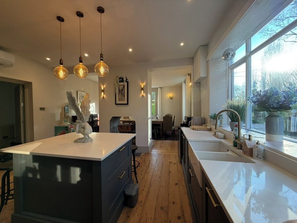 A modern kitchen with pendant lights, a large island, and a view of the outdoors.