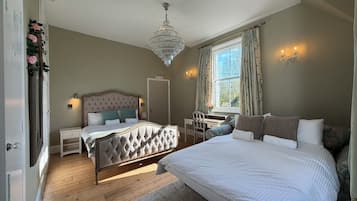 A bedroom with a large bed, a desk, a chair, a chandelier, and a window with curtains.