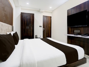 Une chambre d’hôtel moderne avec un grand lit, une armoire en bois, un téléviseur à écran plat et une petite table avec une bouilloire et des tasses.