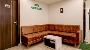 A hotel room with a brown leather sofa, a white side table, and a door labeled 'Green Valley 704'. - Super Deluxe Roomnana Chiloda Near Airport (Gandhinagar)
