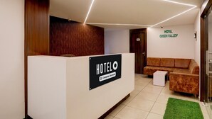 A hotel reception area with a reception desk, a brown sofa, a green rug, and a sign indicating the hotel name. - Super Deluxe Roomnana Chiloda Near Airport (Gandhinagar)