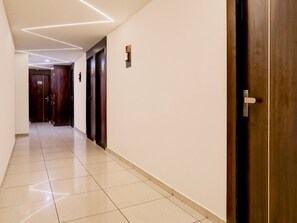 A corridor with a tiled floor, wooden doors, and a wall-mounted light fixture. - Super Deluxe Roomnana Chiloda Near Airport (Gandhinagar)