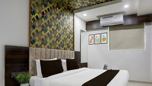 A modern hotel room with a bed, bedside tables, a potted plant, and artwork on the wall. - Super Deluxe Roomnana Chiloda Near Airport (Gandhinagar)