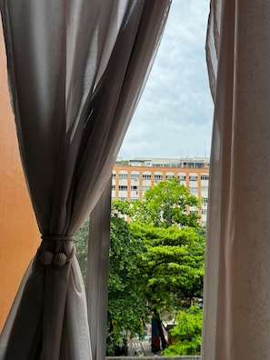 Ein Fenster mit Vorhängen, Blick auf ein Gebäude und etwas Grün.