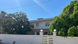 A white building with a tiled roof, a gated entrance, and potted plants along the sidewalk. - Seaside villa with patio, just 250 m / 3 minute walk to the beach (Sicilia)