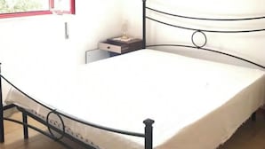 A room with a bed, a nightstand, a hanging lamp, a window with a red frame, and a wall-mounted picture. - Seaside villa with patio, just 250 m / 3 minute walk to the beach (Sicilia)