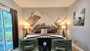 Una camera da letto con un letto, due abat-jour, un quadro, una finestra e vista sull'esterno.