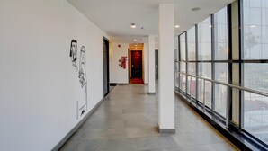 A modern hotel corridor with a tiled floor, large windows, and a red door at the end. - Deluxe BSA Townhouse (Lucknow)