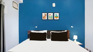 A bedroom with a blue accent wall, a bed with black and white bedding, two framed artworks, a nightstand with a lamp, and a window with curtains. - Super Hotel O Noonmati Guwahati (Guwahati)