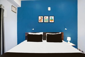 A bedroom with a blue accent wall, a bed with black and white bedding, two framed artworks, a nightstand with a lamp, and a window with curtains. - Super Hotel O Noonmati Guwahati (Guwahati)