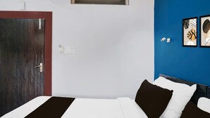 A hotel room with a wooden door, a bed with white and brown bedding, a blue accent wall, and two framed artworks. - Super Hotel O Noonmati Guwahati (Guwahati)