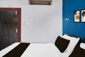 A hotel room with a wooden door, a bed with white and brown bedding, a blue accent wall, and two framed artworks. - Super Hotel O Noonmati Guwahati (Guwahati)