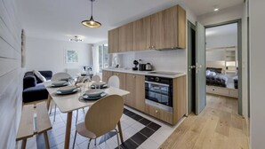 Una cocina moderna con armarios de madera, un comedor con mesa y sillas, y vistas hacia un dormitorio con cama.