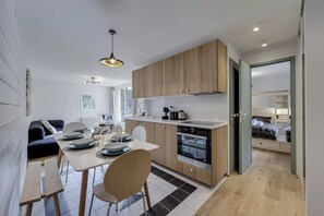 A modern kitchen with wooden cabinets, a dining area with a table and chairs, and a view into a bedroom with a bed. - Oréades 101, sunny Renovated Apartment with Balcony, Central Val d’Isère (Val-d'Isère)