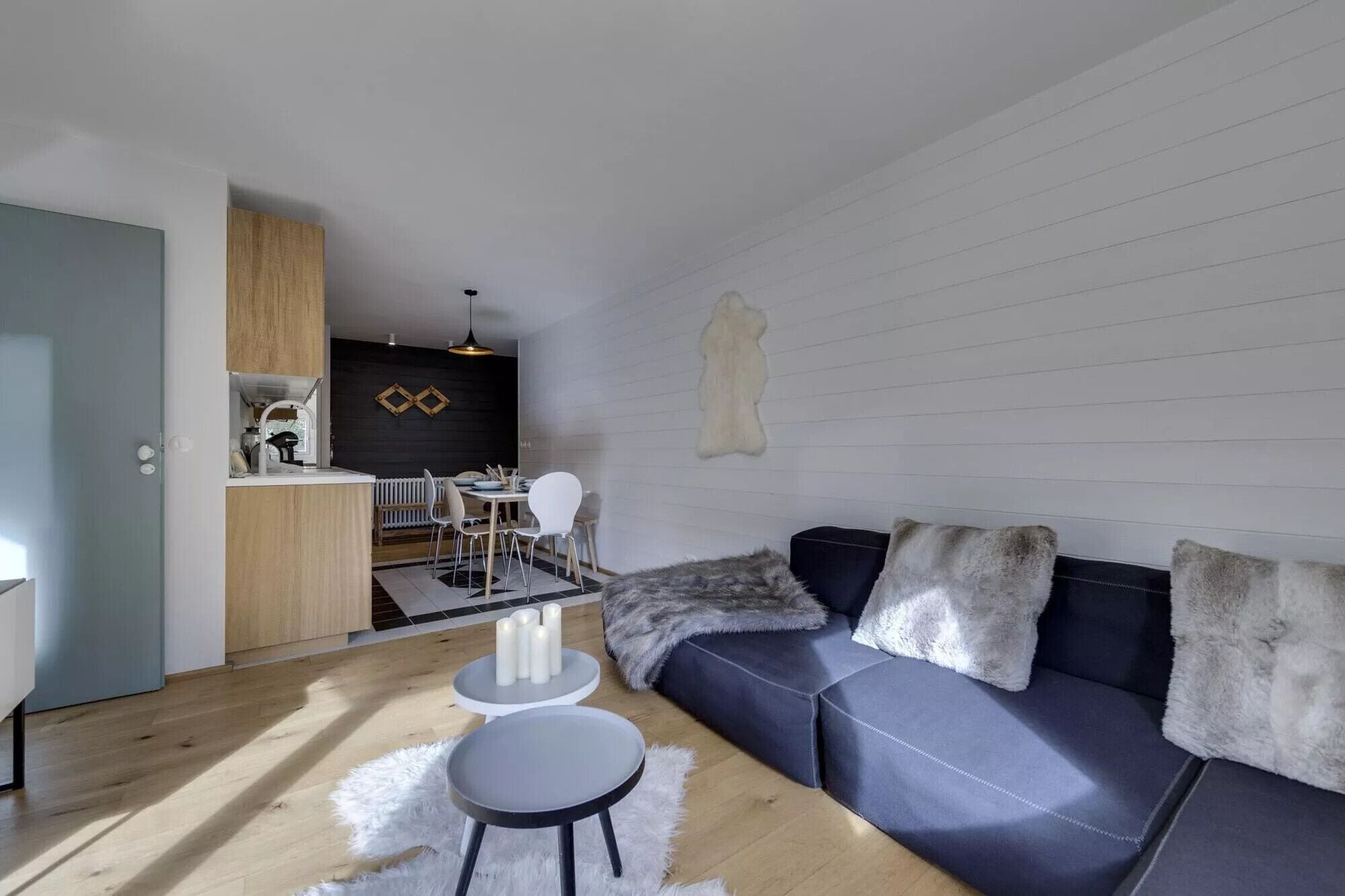 A modern living room with a sofa, a dining table, and a kitchen area.