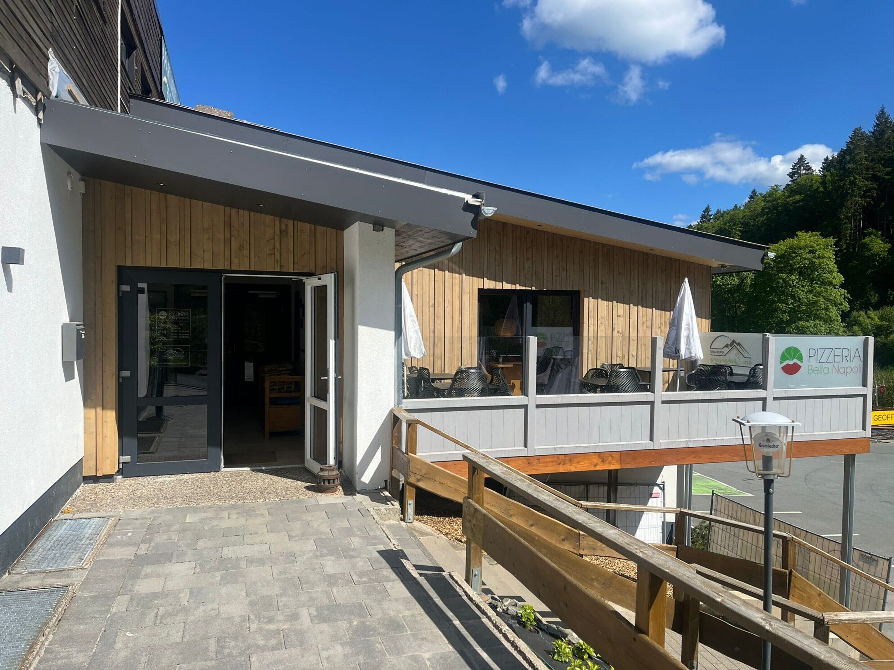 A pizzeria with a wooden exterior, a covered outdoor seating area, and a paved entrance.