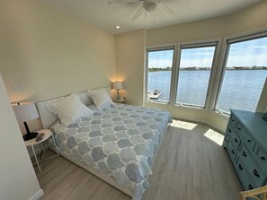 Un dormitorio con cama, mesitas de noche, cómoda y vista a una masa de agua a través de amplias ventanas.