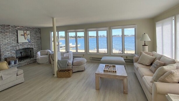 Ein Wohnzimmer mit Kamin, großen Fenstern mit Meerblick, einer Couch und einem Couchtisch.