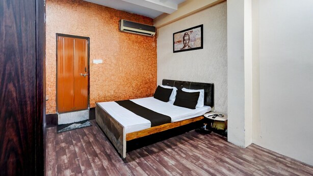 A bedroom with a wooden bed, a door, an air conditioner, and a framed picture on the wall. - Super Lokmanya Formerly Siddhivinayak (Nagpur)