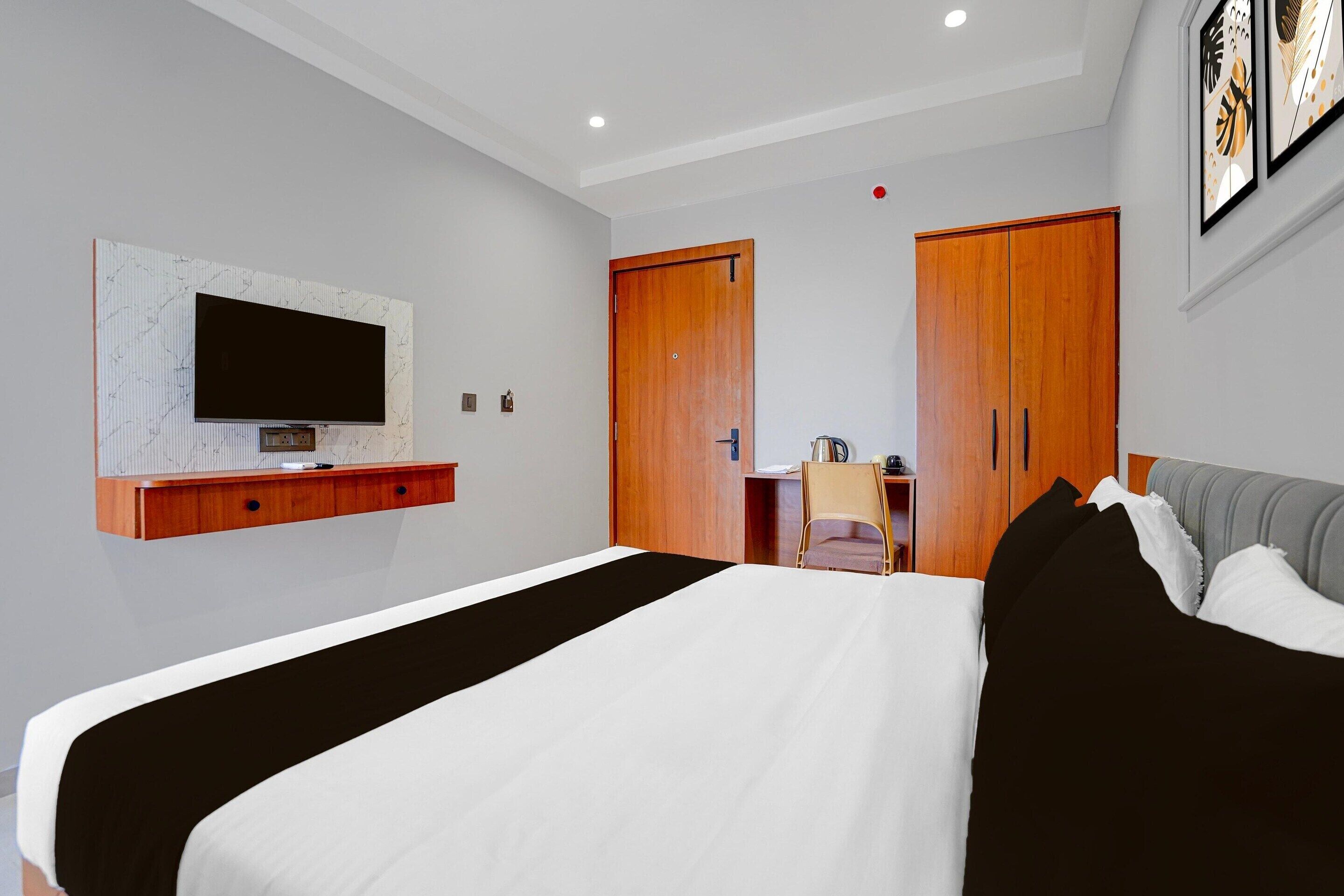 Ein modernes Hotelzimmer mit einem großen Bett, einem flachbildfernseher an der Wand, einem Holzschrank und einem Schreibtisch mit Stuhl.