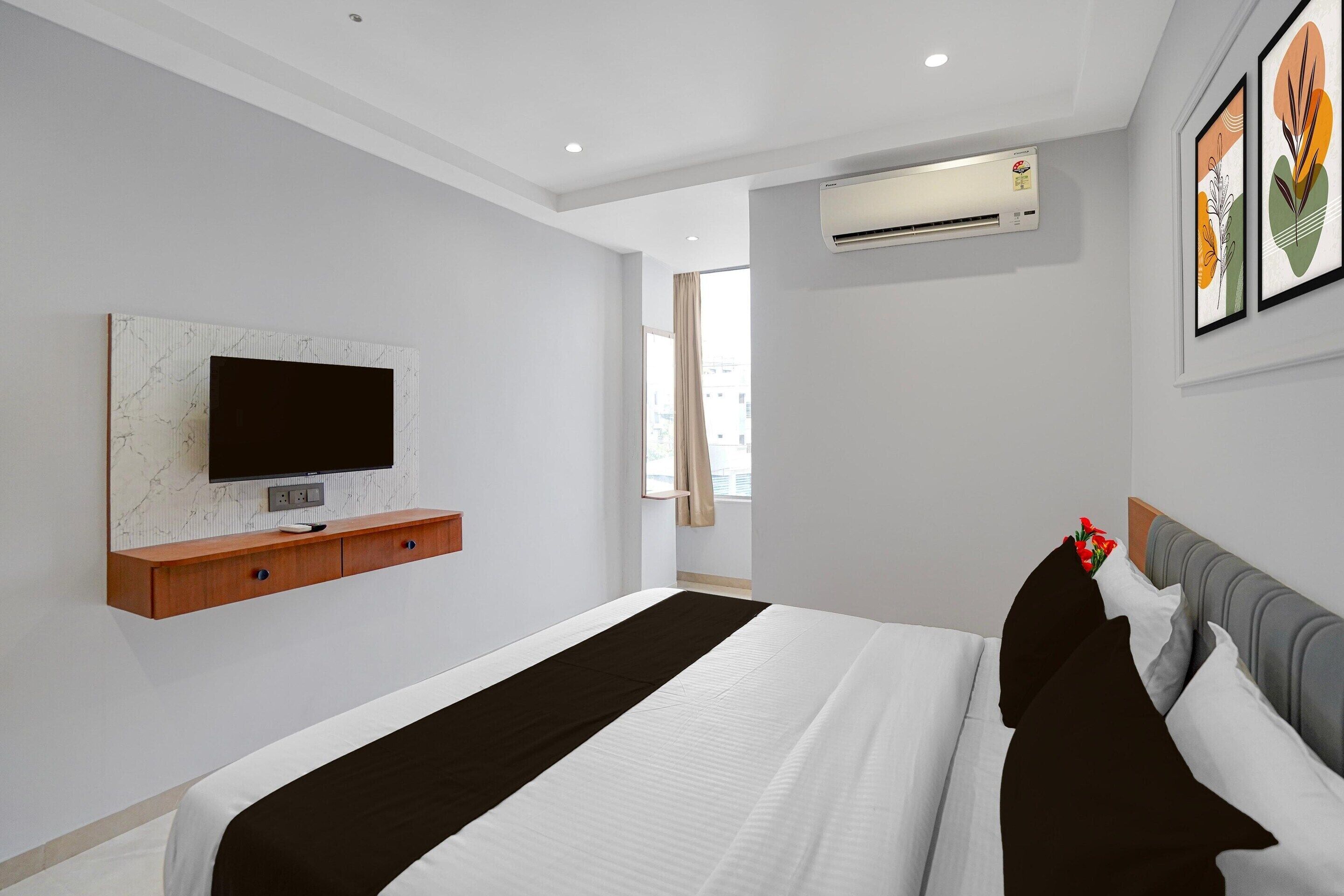 Et moderne hotelværelse med en stor seng, et vægmonteret TV, en aircondition og et vindue med gardiner.
