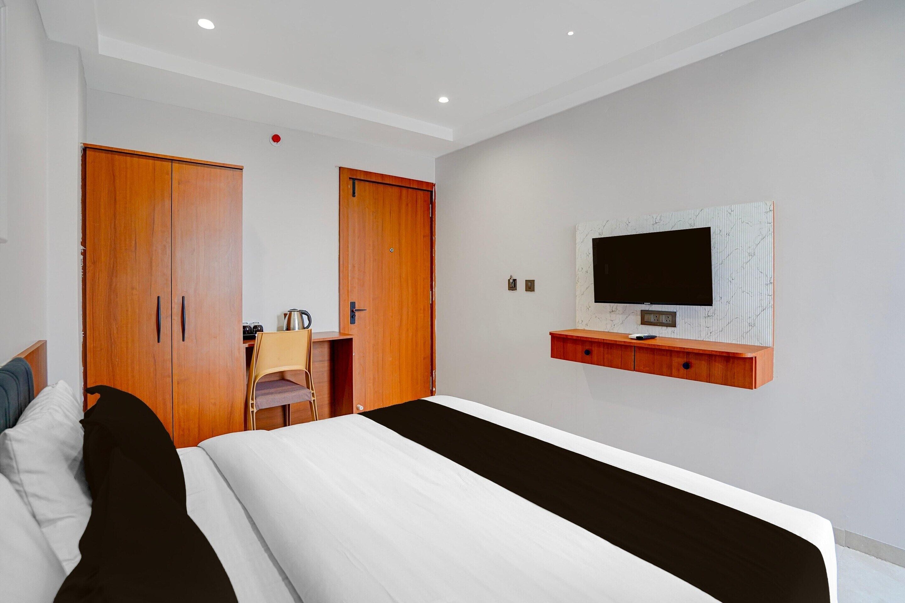 Una camera d'albergo con un letto, una scrivania, una sedia, un armadio e una televisione a muro.