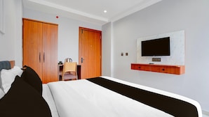 Een hotelkamer met een bed, een aan de muur bevestigde televisie, houten kasten en een bureau met een stoel.