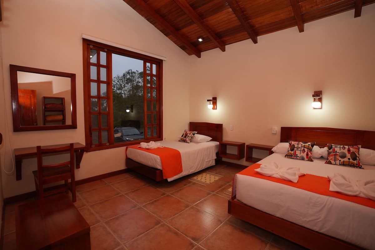 A hotel room with two beds, a wooden ceiling, a large window, and a mirror on the wall.