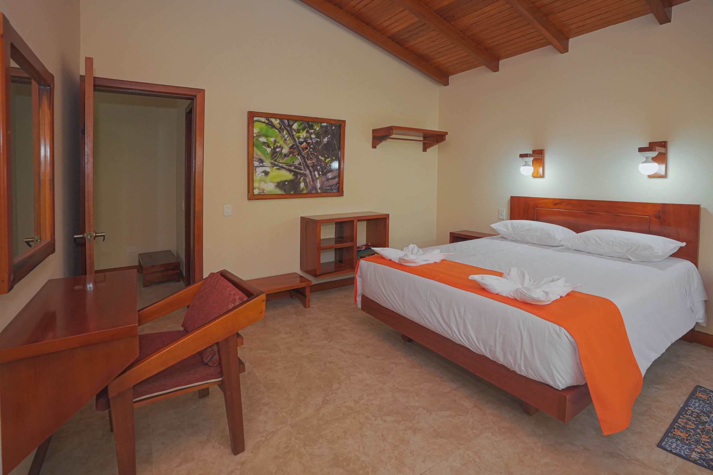 Un dormitorio con cama de madera, escritorio, silla, mesita de noche y estante en la pared.