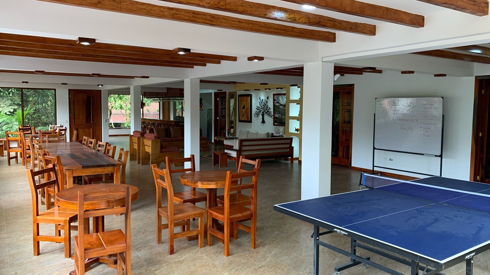 Un espai interior ampli amb diverses taules i cadires de fusta, una taula de ping-pong i una pissarra penjada a la paret.