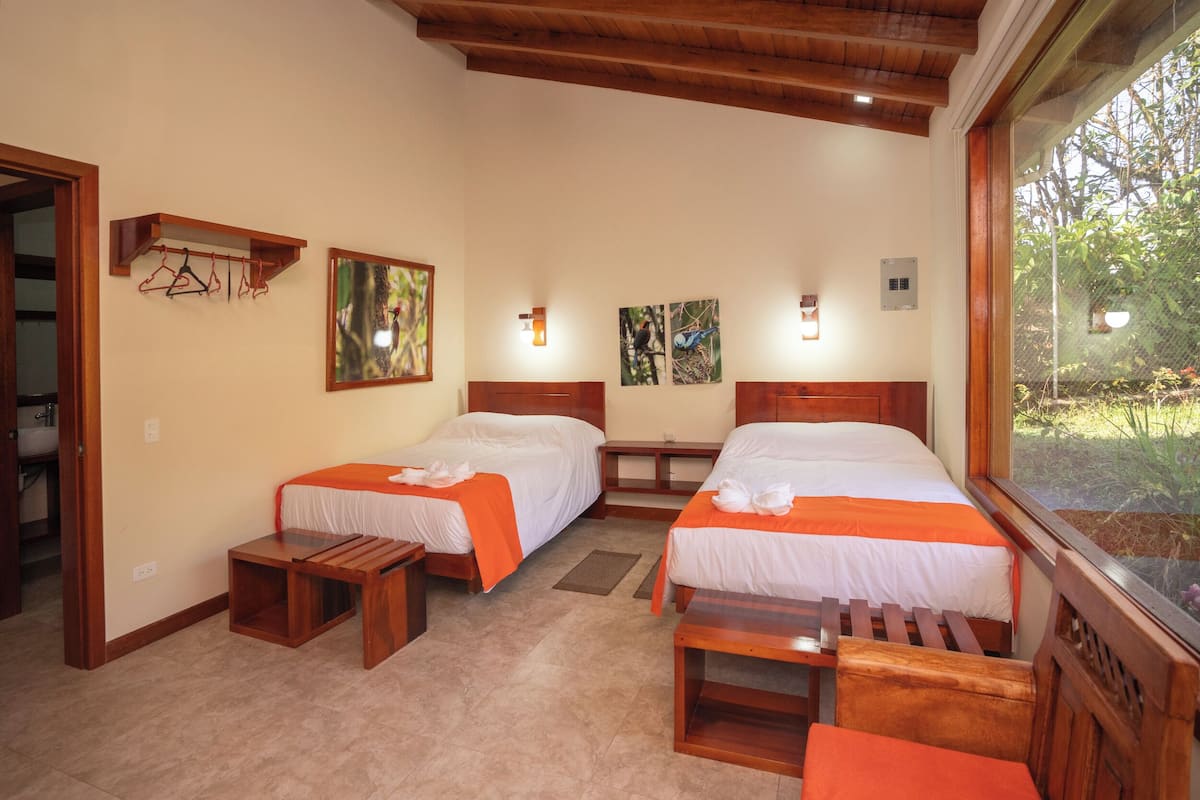 A room with two beds, wooden headboards, a small table, and a bench.
