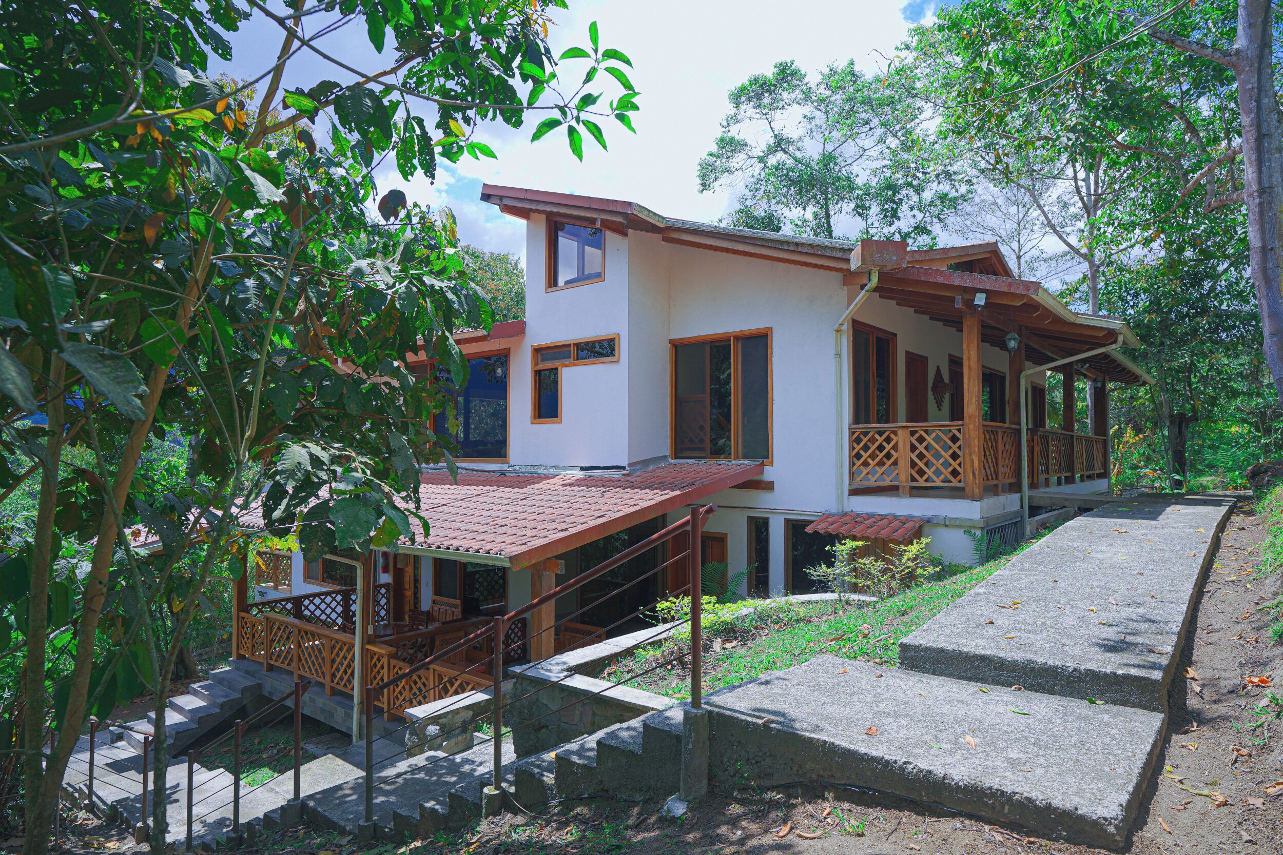 Uma casa de dois andares com varanda, escadaria e um pequeno jardim.