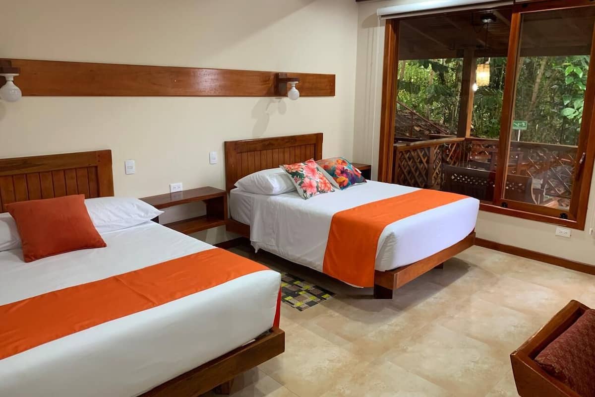 A hotel room with two beds, wooden headboards, a large window with a view of greenery, and a wooden ceiling.