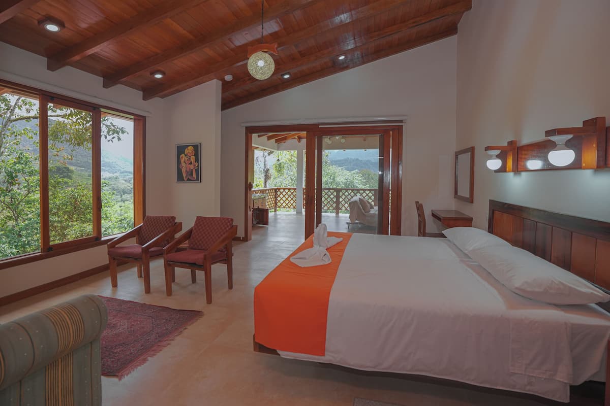 A hotel room with a large bed, wooden ceiling, large windows, and a balcony with a view.