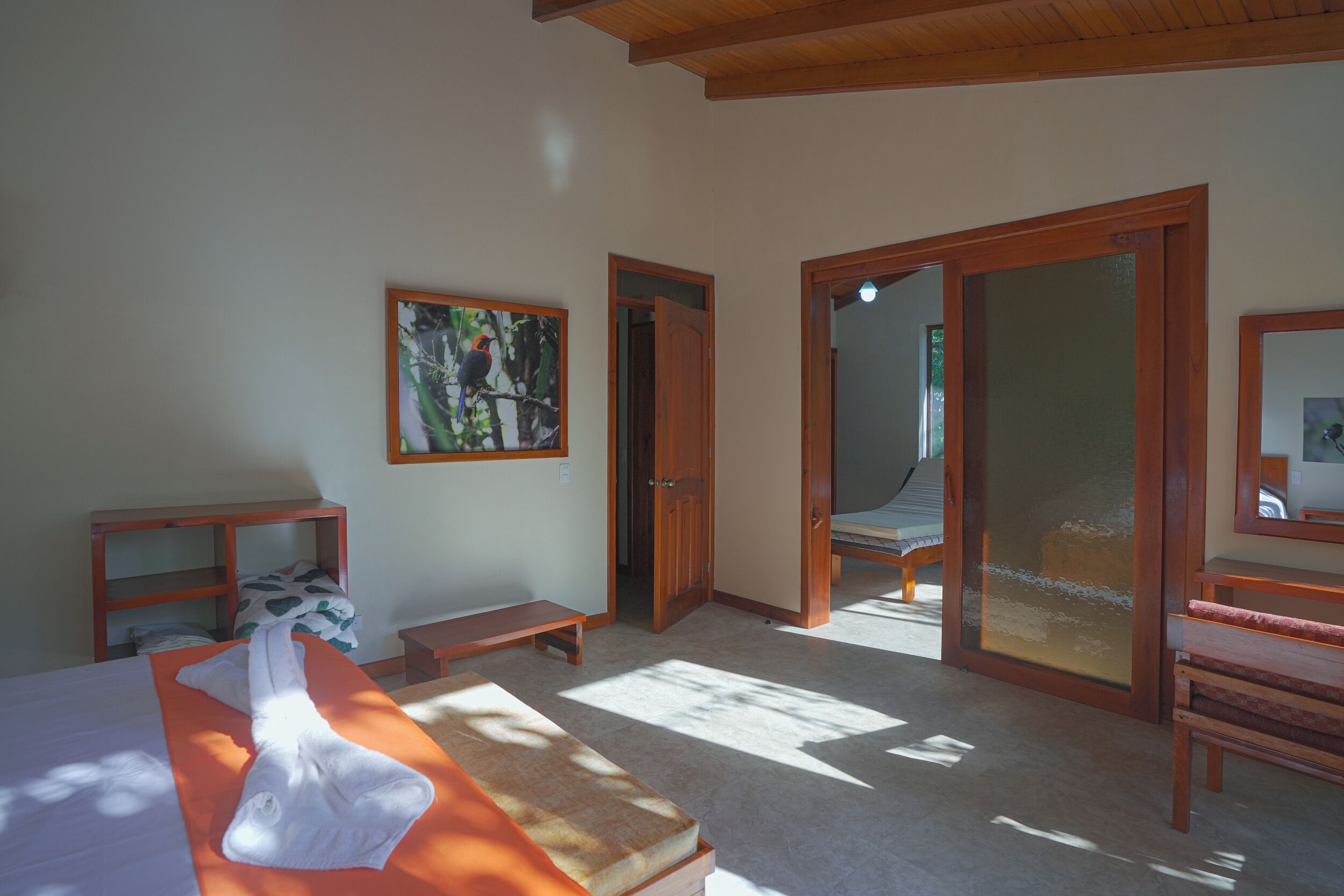 A room with a bed, a bench, a small table, and a door leading to another room.