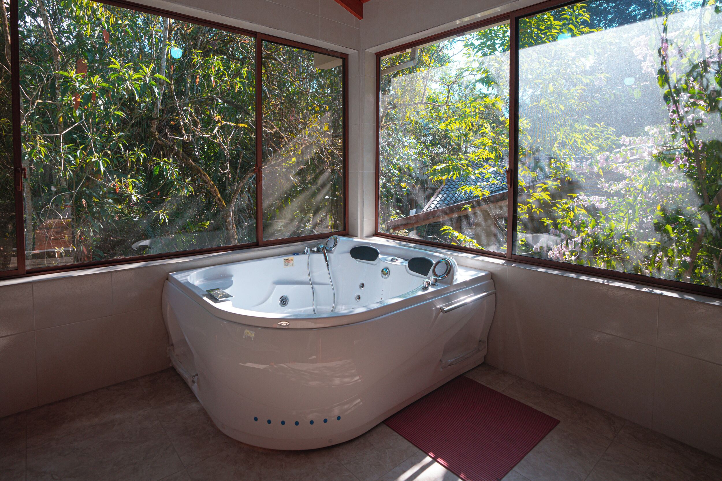 A modern bathroom with a large bathtub, large windows, and a view of trees and a building outside.