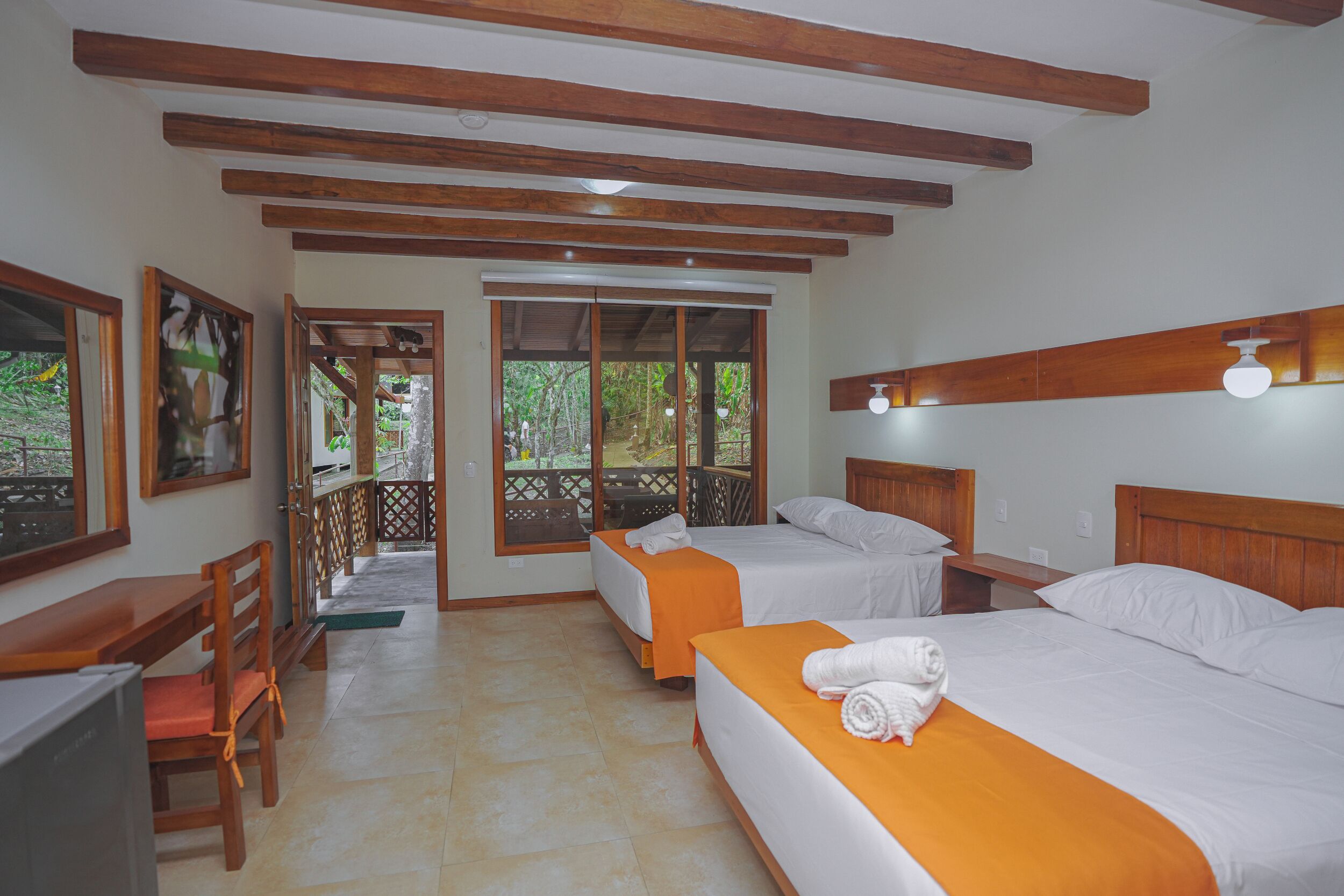 A hotel room with two beds, wooden beams, a desk, and a TV.