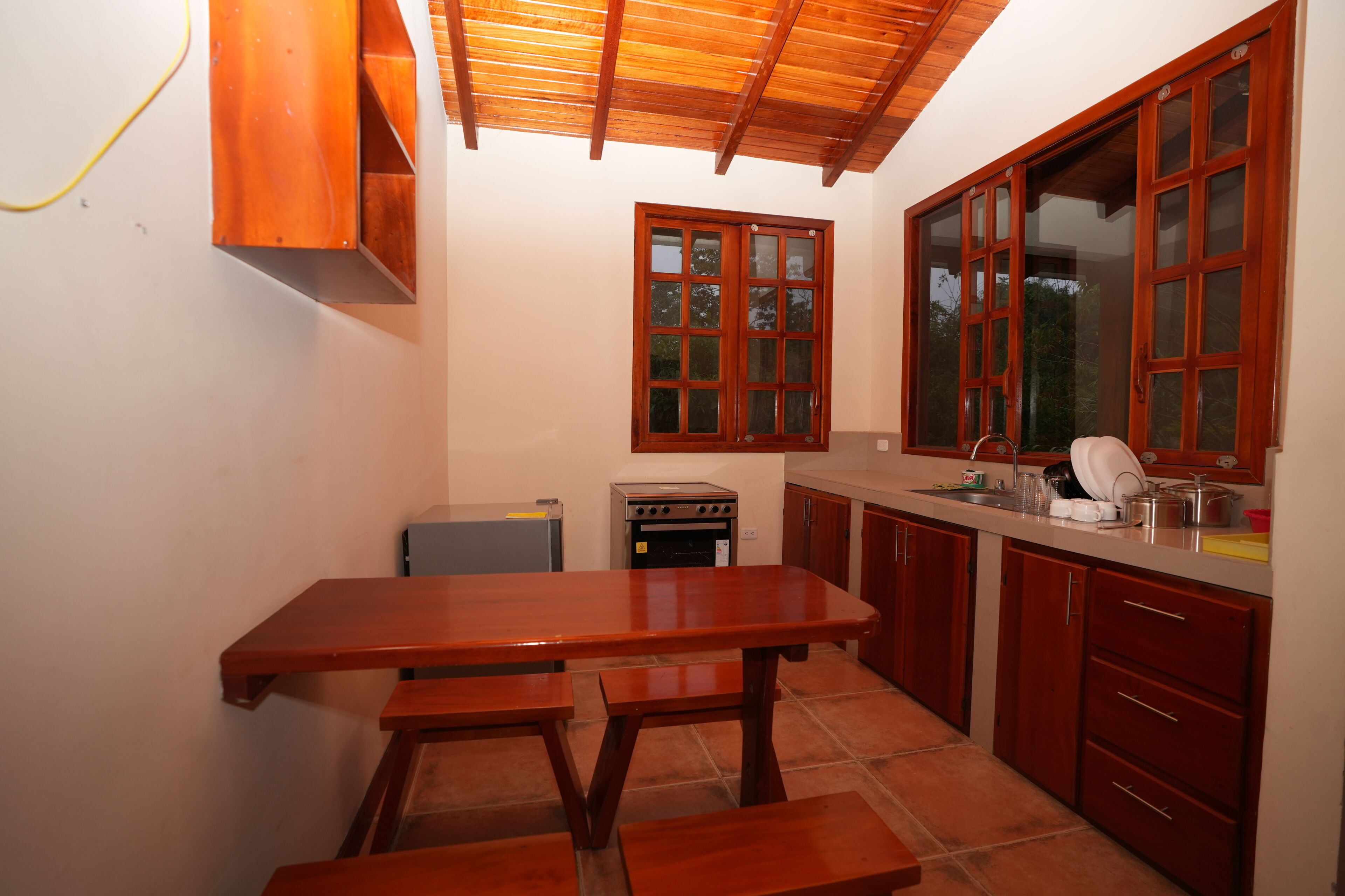 A kitchen with wooden cabinets, a tiled floor, a wooden table, and a window with a view.