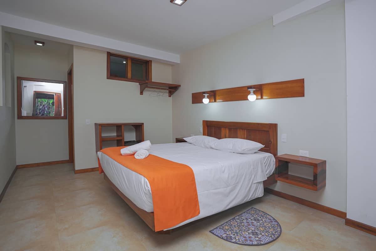 A bedroom with a bed, a nightstand, a wooden shelf, a mirror, and a patterned rug.