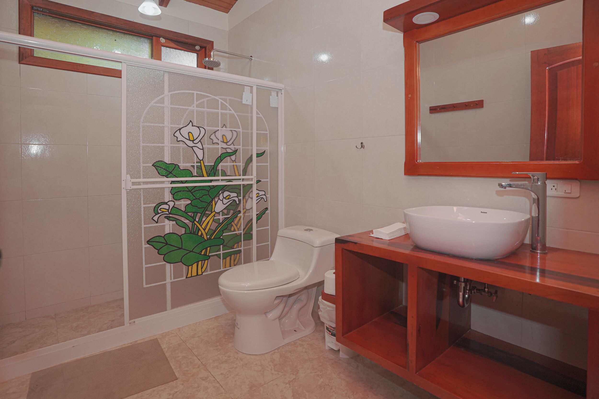 Un baño con inodoro, un lavamanos blanco, un espejo y un box de ducha con puerta de vidrio.